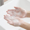 Hands are covered in white soap lather while washing under a faucet.