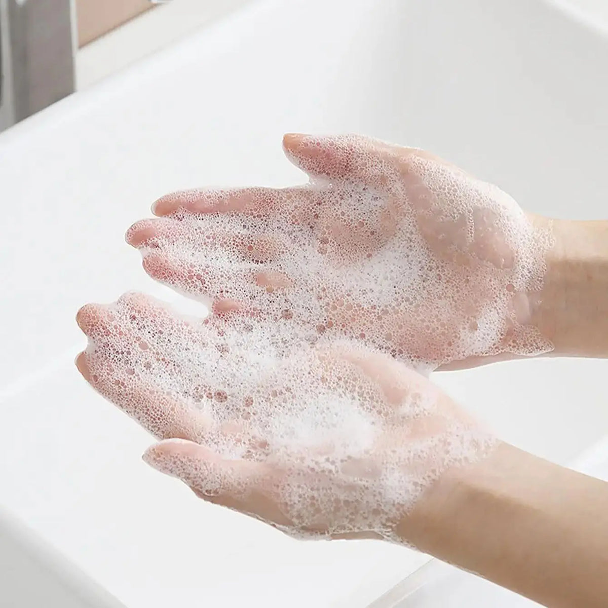 Hands are covered in white soap lather while washing under a faucet.