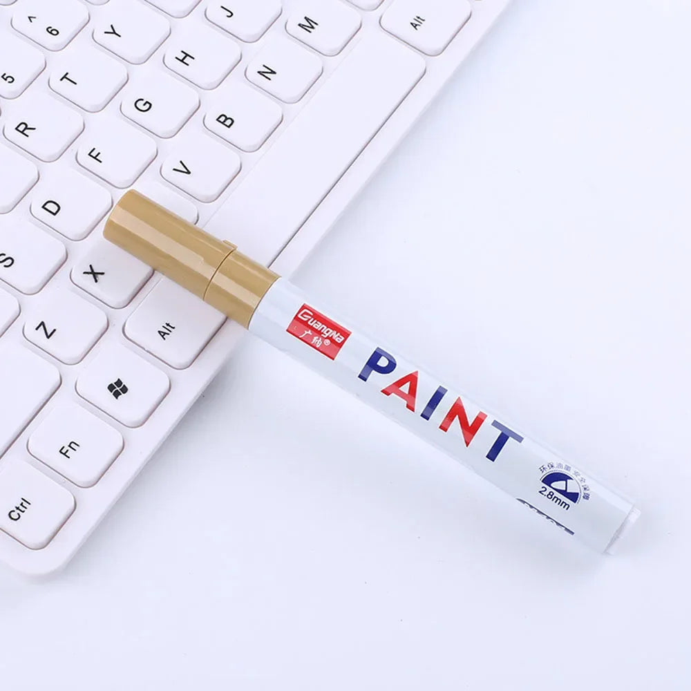 A paint marker pen with a gold cap is placed on a white keyboard.