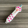 A white retractable cat paw utility knife with pink accents is shown on a wooden surface.