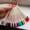 A hand holds a clear acrylic false nail tips kit with various colored tips, displaying them for practice or display.