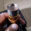 A close-up of a stainless steel high-pressure washer nozzle with a brass quick connect fitting being held in a hand.