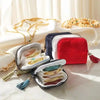 A red velvet jewelry organizer bag with a black zipper and tassel is shown open, displaying various gold and silver jewelry p