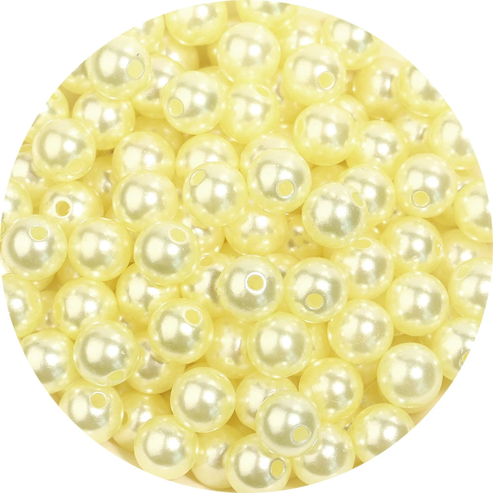 A close-up view of small, round, pale yellow imitation pearl beads for jewelry making.