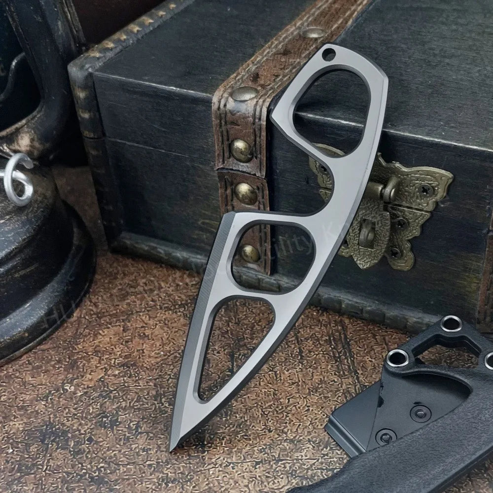 A compact stainless steel neck knife with a distinctive blade design resting on a wooden box and a dark surface.
