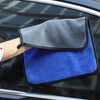 A hand holds a gray and blue microfiber car drying towel with a black trim, positioned against a car window.
