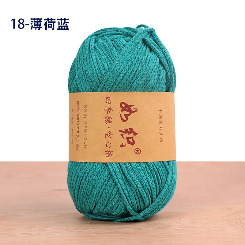 A skein of teal cotton blend crochet yarn is shown on a wooden surface.