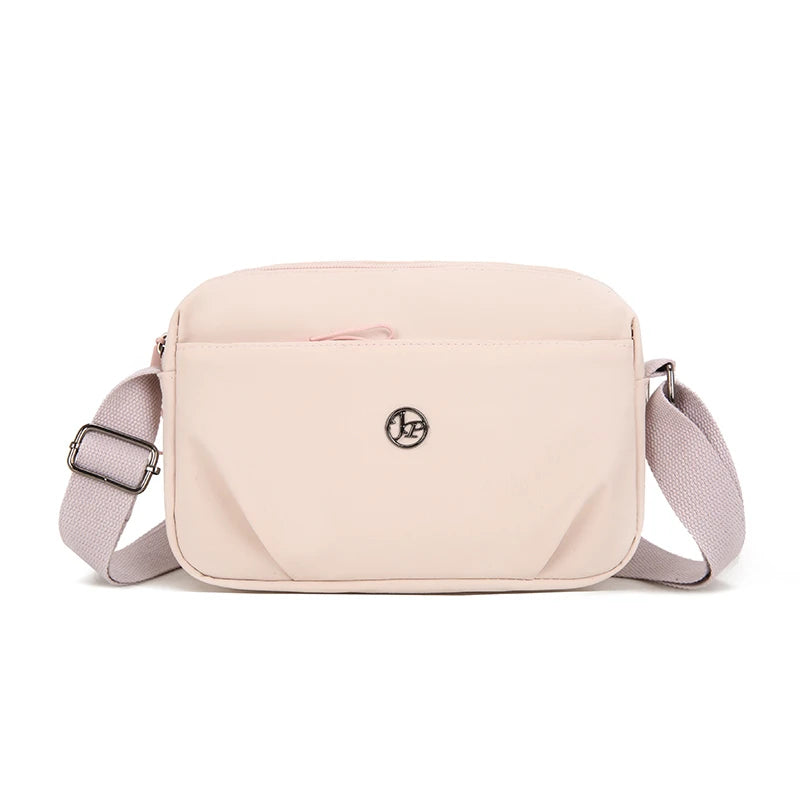 A light pink nylon crossbody bag with a flap and strap is shown against a white background.