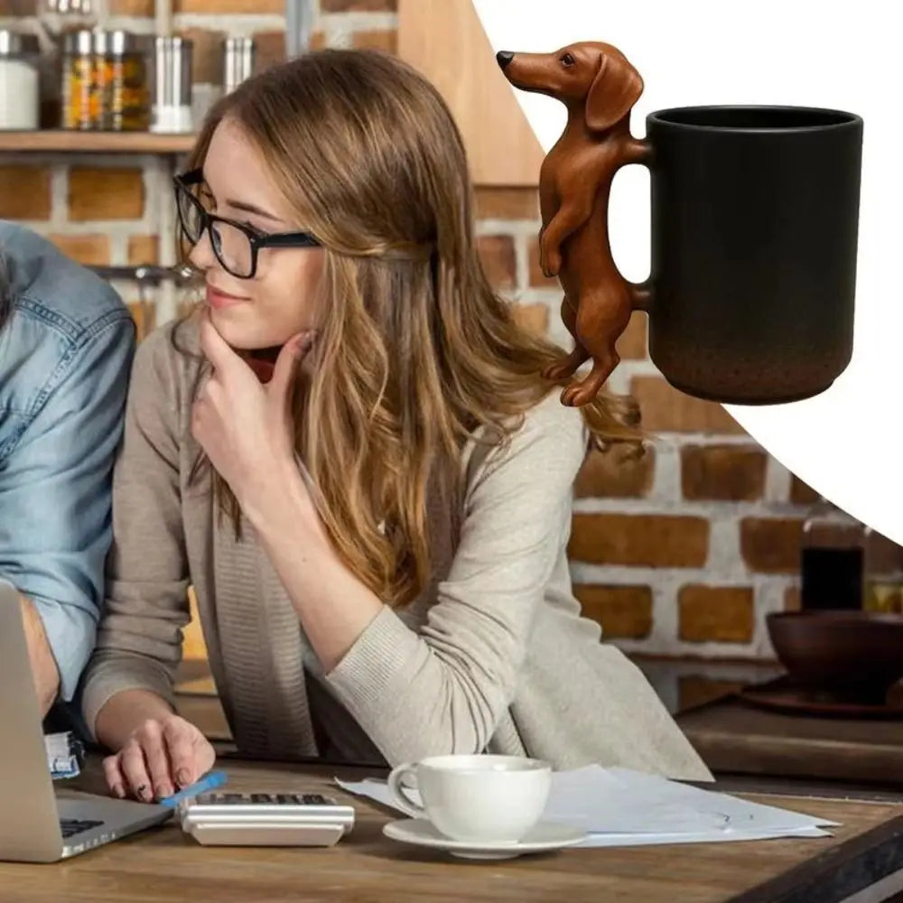 A woman sits at a wooden table with a dark coffee mug and papers, featuring a dachshund puppy handle.