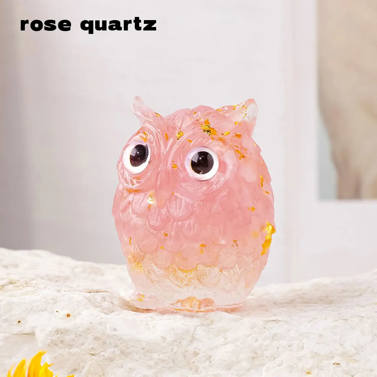 A handcrafted rose quartz crystal owl figurine with a natural crushed stone finish sitting on a light surface.