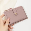 A hand holds a light pink slim PU leather card holder wallet with a stitched flap and gold hardware.
