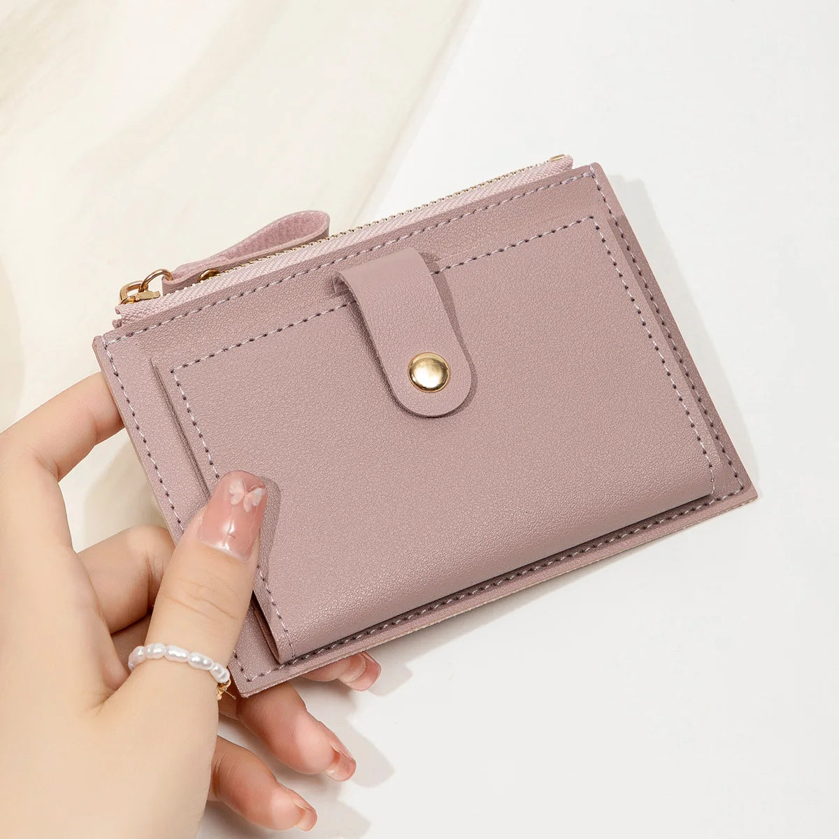 A hand holds a light pink slim PU leather card holder wallet with a stitched flap and gold hardware.