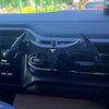 A black gravity car phone holder is installed in a vehicle's air vent, designed to secure a phone.