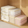 A set of clear mesh storage bags for clothes, blankets, and bedding stacked on a wooden shelf.