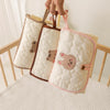 Three quilted beige and pink foldable portable diaper changing pads being held by a hand.