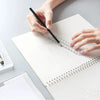 A hand is using a black pen to mark a transparent plastic ruler on a white notebook for measuring.