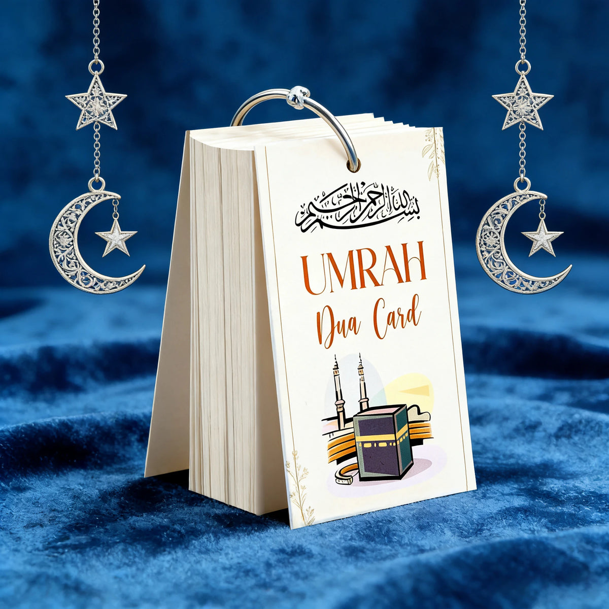A set of portable Islamic Umrah Dua cards with hanging charms displayed on a dark blue velvet surface.