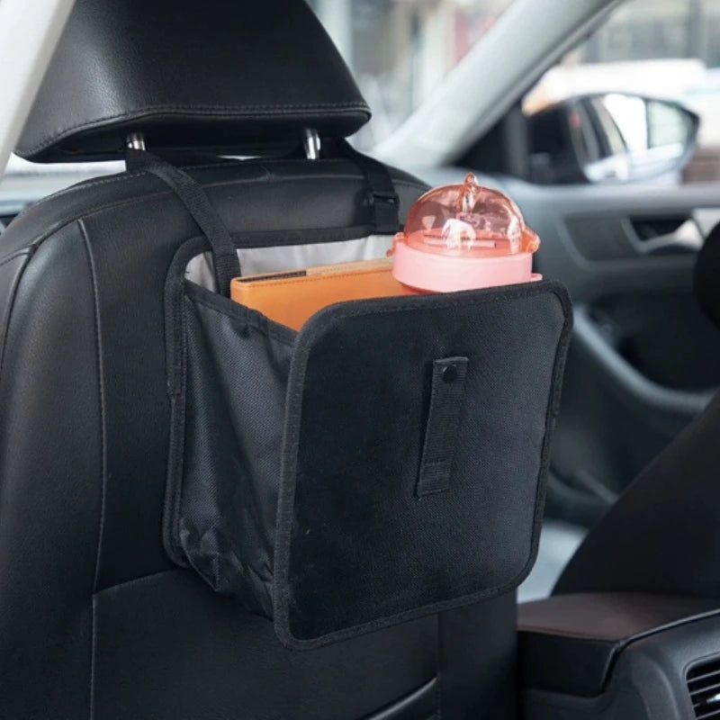 A black fabric organizer is placed on a car seat, holding a pink glass and a small orange item.