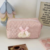 A pink quilted cosmetic pouch with a sheer lace bow trim resting on a white surface.