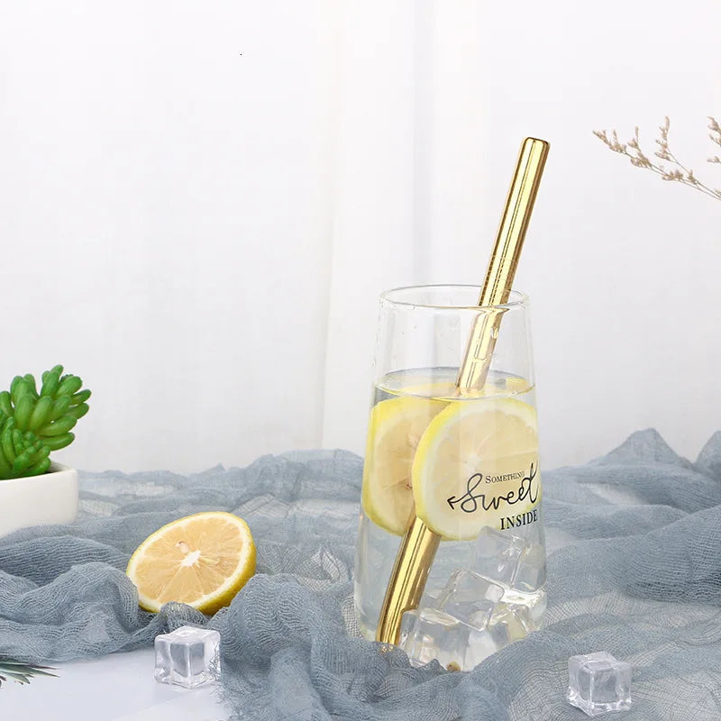 A glass of lemon-infused water with a gold drinking straw and cleaning brush resting on a gray cloth.