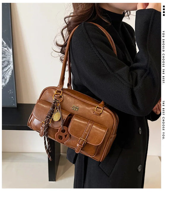 A woman holds a brown retro PU leather shoulder bag with multiple pockets and a leather charm against a black turtleneck swea
