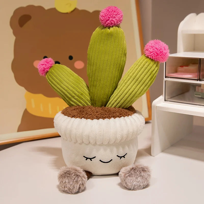 A cute artificial flower plush doll resembling a cactus with green body and pink fuzzy flowers sitting in a white pot.