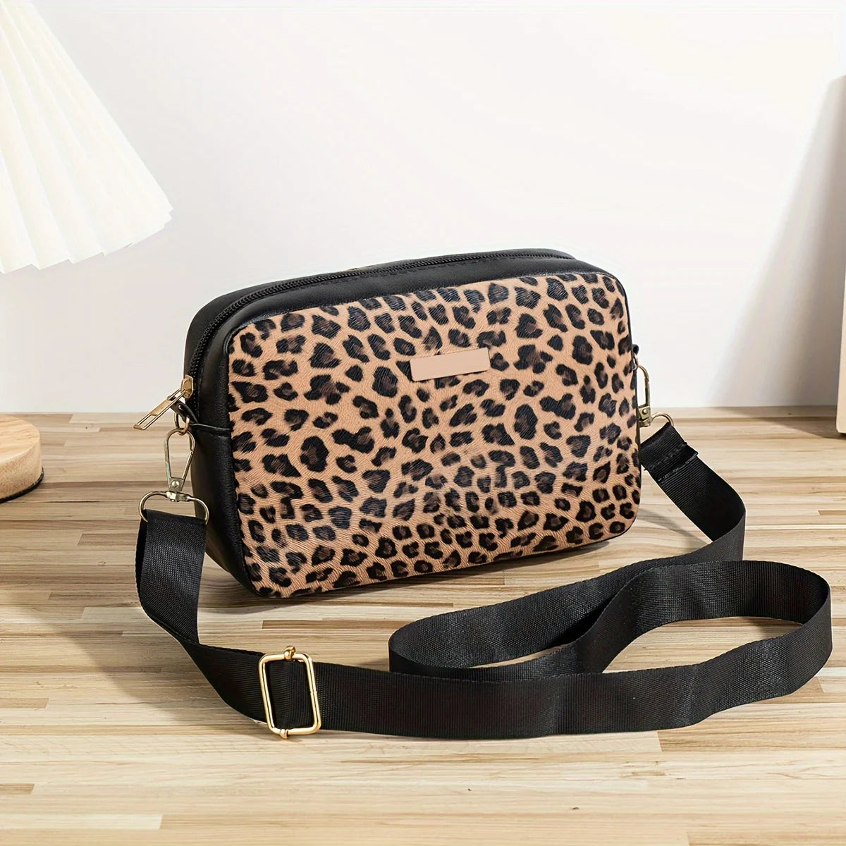 A black leopard print crossbody bag with a gold buckle strap resting on a wooden surface.