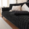 A black quilted sofa cushion cover with white pillows and a dark leather sofa in a bright room.