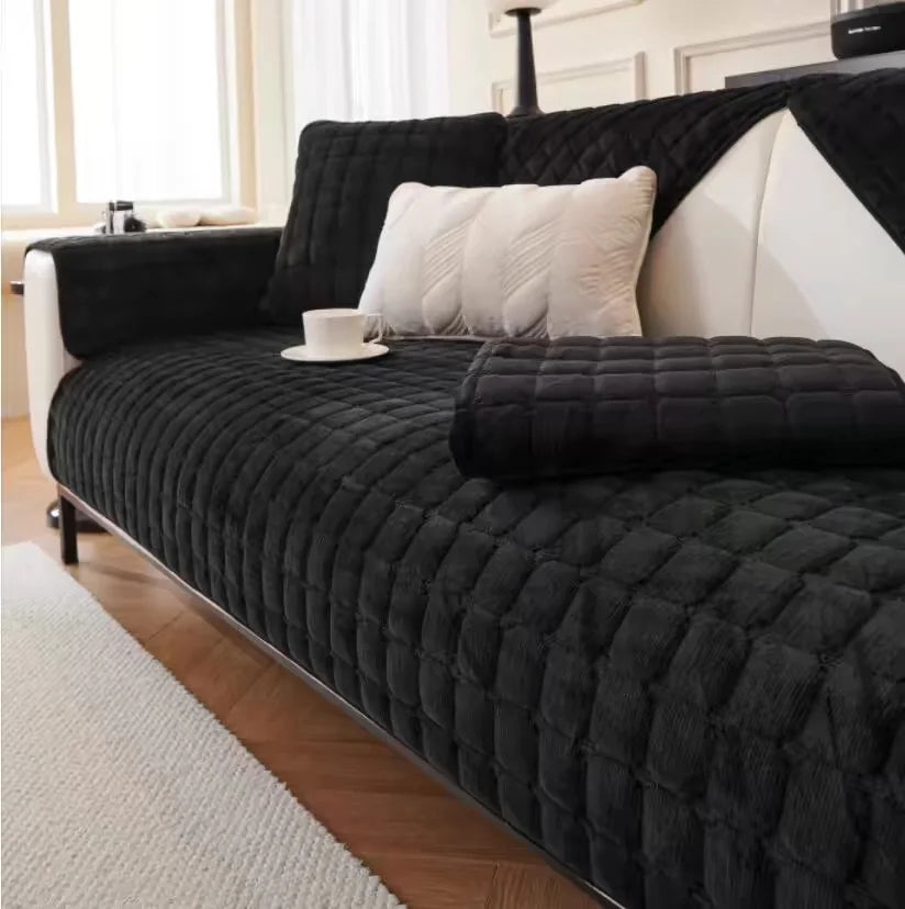 A black quilted sofa cushion cover with white pillows and a dark leather sofa in a bright room.