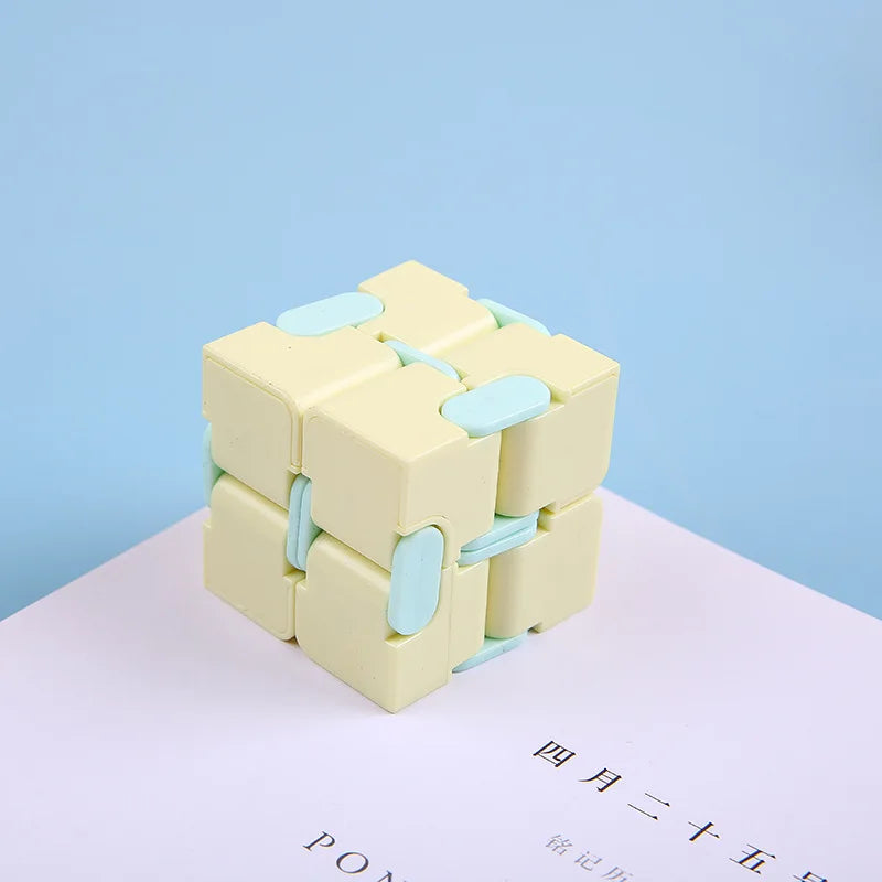 A light yellow infinity magic cube fidget toy with light blue accents resting on a white surface.