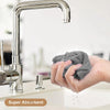 A hand is using a silver kitchen faucet to pour water onto a gray microfiber cloth for cleaning.