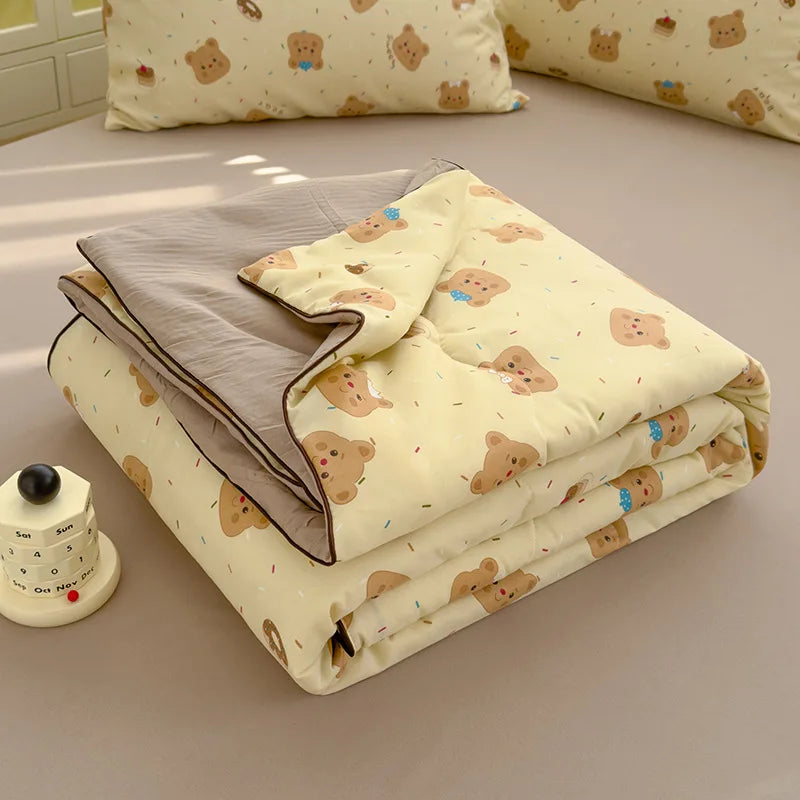 A folded lightweight washed cotton summer quilt in pale yellow with brown animal print on a beige surface.