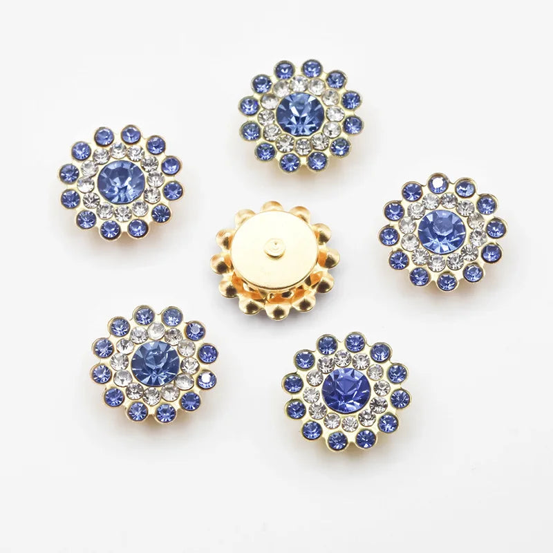 A collection of twelve round, blue and clear rhinestones set in flower shapes on a gold-toned base.