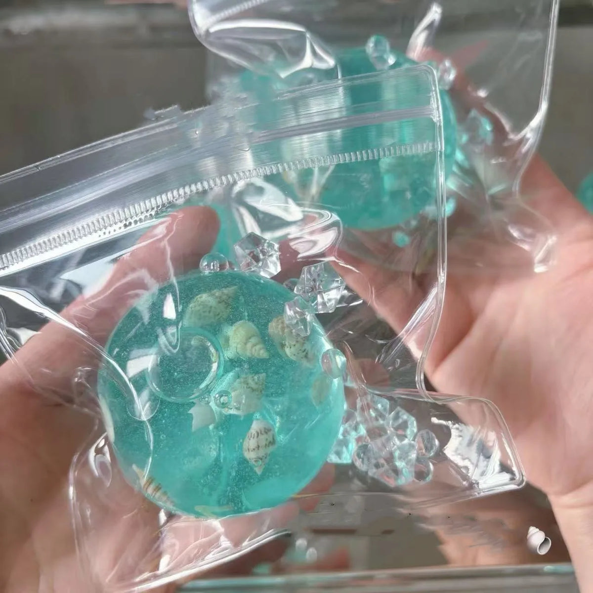 A hand holds a clear plastic bag filled with teal and green ocean squishy stress balls.