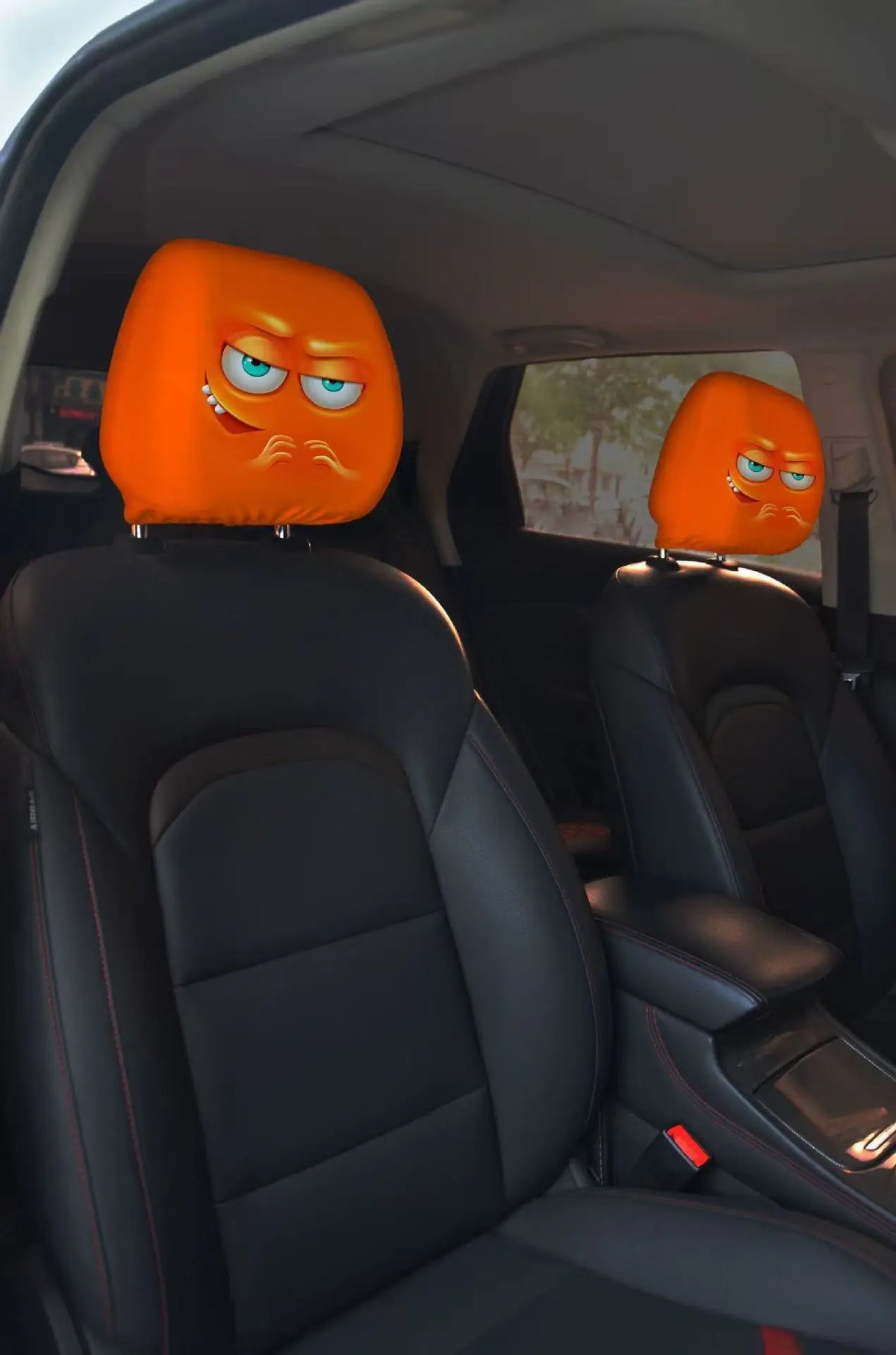 A pair of orange horror-themed car headrest covers with creepy face designs installed in a vehicle interior.