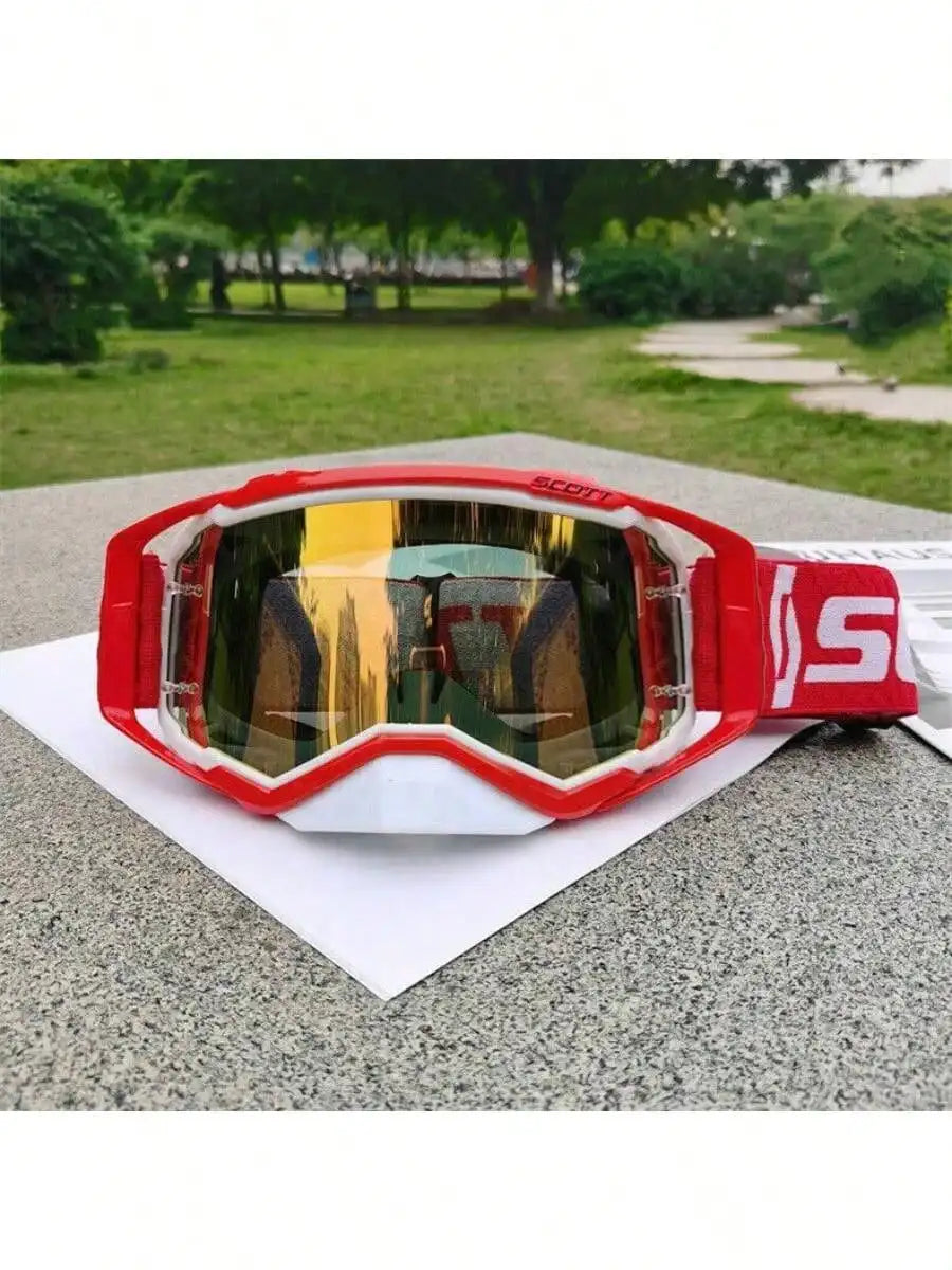 A pair of red and orange motocross goggles resting on a white paper on a gray surface.