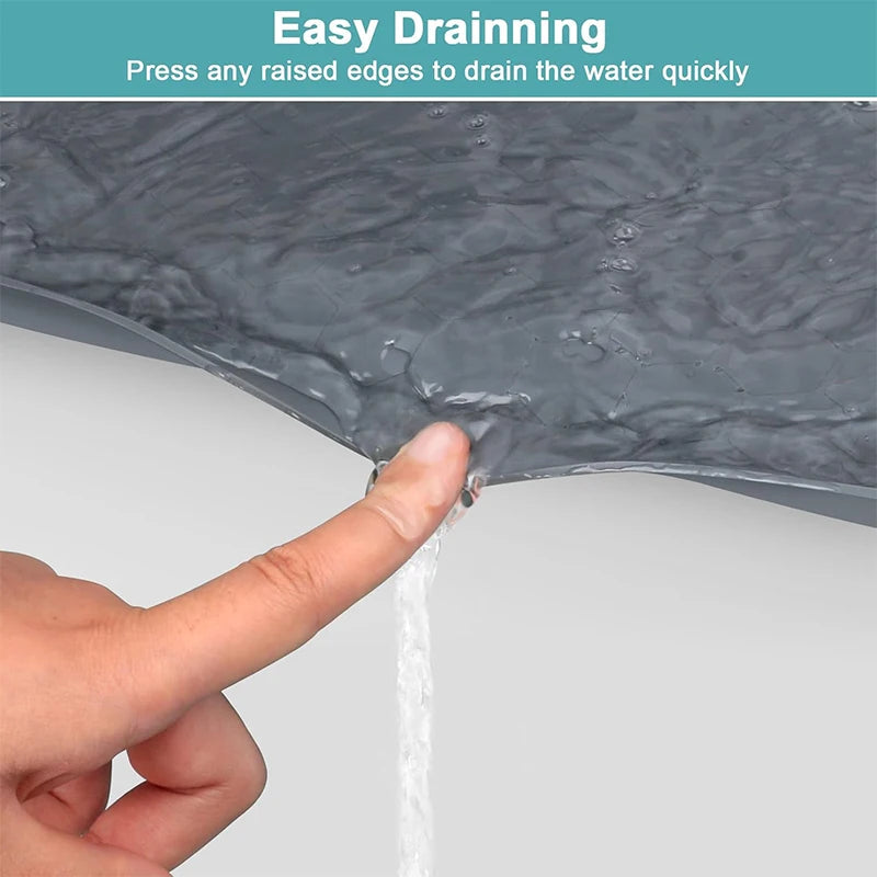 A hand is pressing a raised edge on a dark gray silicone mat to drain water quickly.