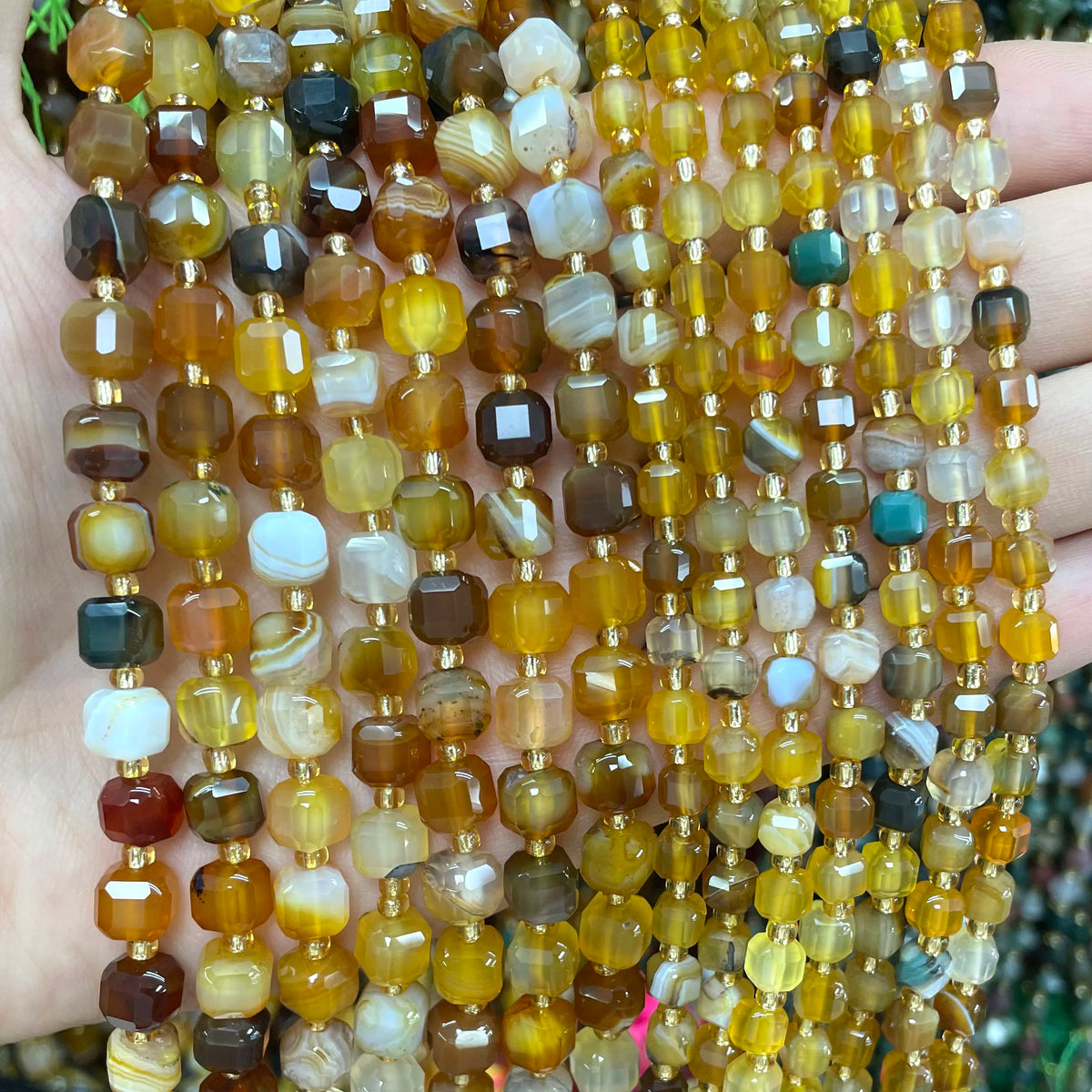 A close-up of a strand of natural square faceted beads in various shades of amber, brown, and green stones for jewelry making