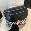 A black multi-pocket PU leather waist bag with a silver zipper is held by a hand against a white surface.