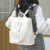 A woman is wearing a cream leather backpack with silver zippers and a white checkered shirt.