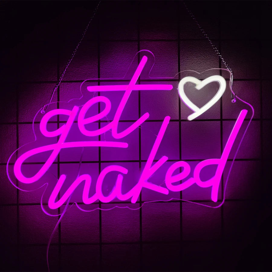 A neon sign glows bright pink purple with the text get naked and a heart shape on a dark background.