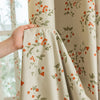 A close-up of a beige blackout curtain panel featuring an orange and green plant pattern.