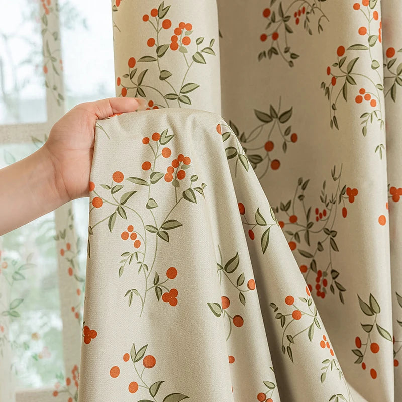 A close-up of a beige blackout curtain panel featuring an orange and green plant pattern.