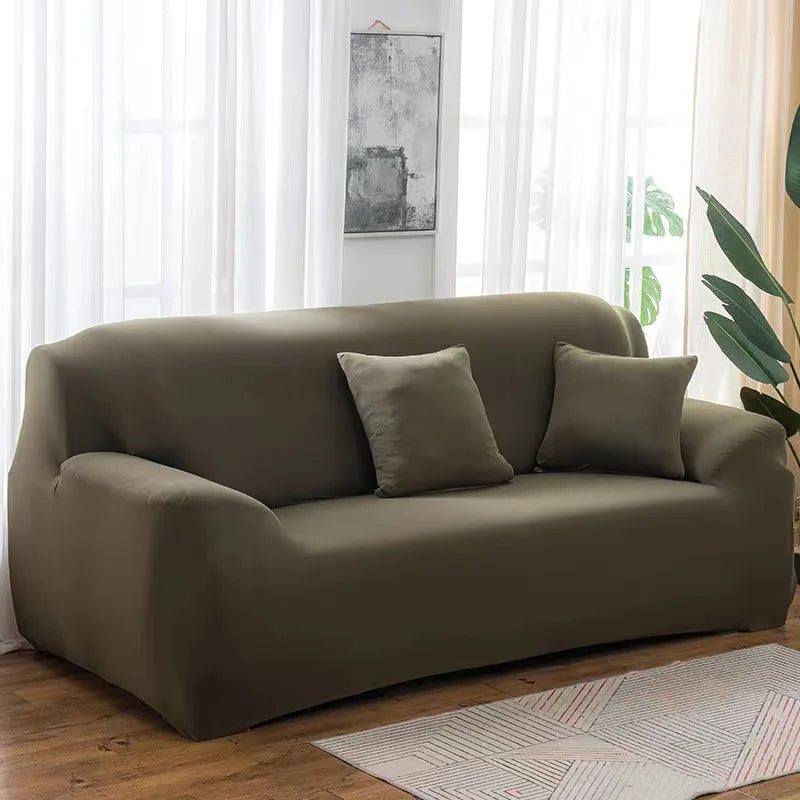 A modern, taupe elastic stretch sofa cover is displayed indoors next to a window.