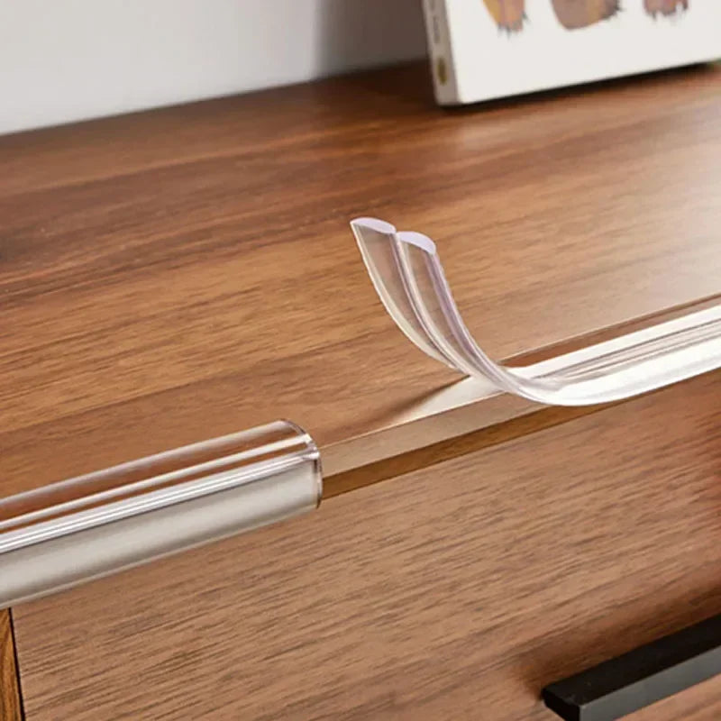 Nahaufnahme transparenter PVC-Sicherheitsstreifen, die auf die Kante eines Holztisches oder Möbelstücks aufgebracht werden.