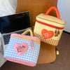 A yellow insulated lunch bag with a red trim and a heart-shaped cartoon design rests next to a pink checkered lunch bag.
