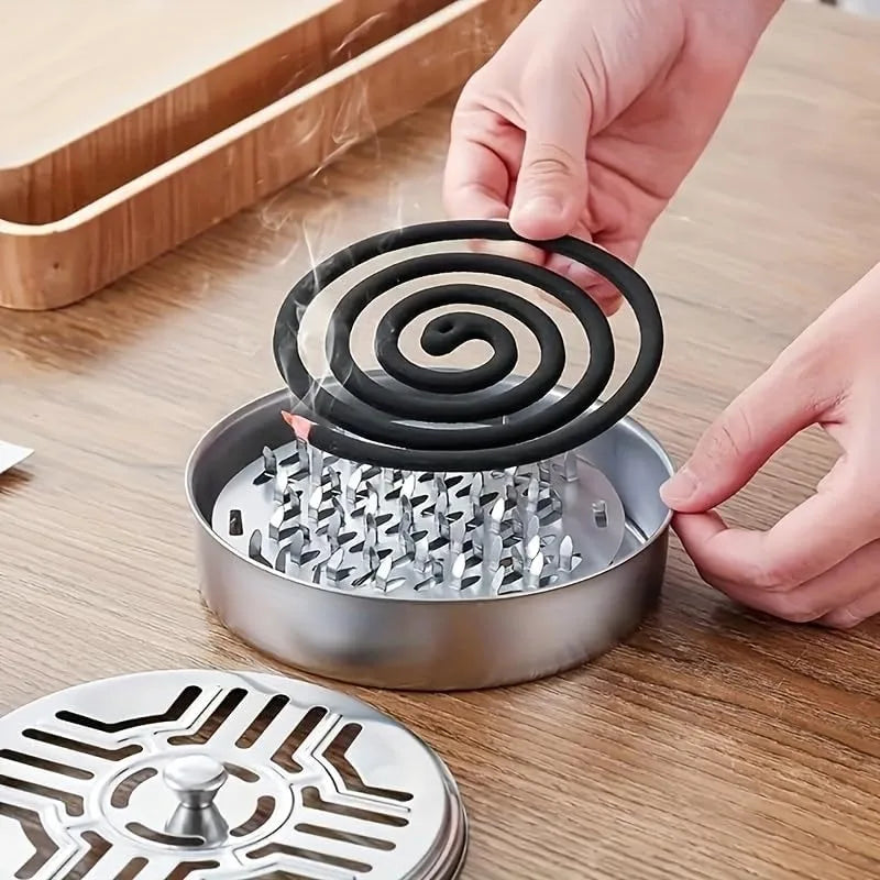 A hand is placing a coiled mosquito coil into a stainless steel holder for burning.