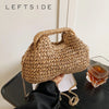 A woven straw chain crossbody handbag is held against a dark surface next to an amber glass.