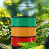 A stack of ten colored filament spools rests on a dark rock with corn stalks and green leaves.