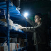 A man uses a Wuben G5 flashlight to illuminate a shelf in a dark warehouse setting.